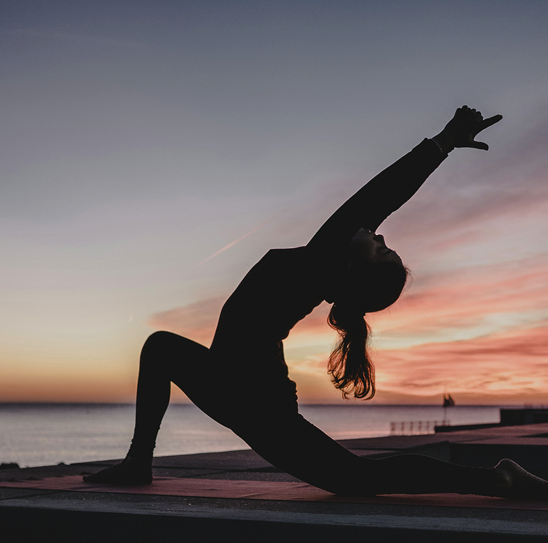 Woman in a yoga pose at sunset by the sea